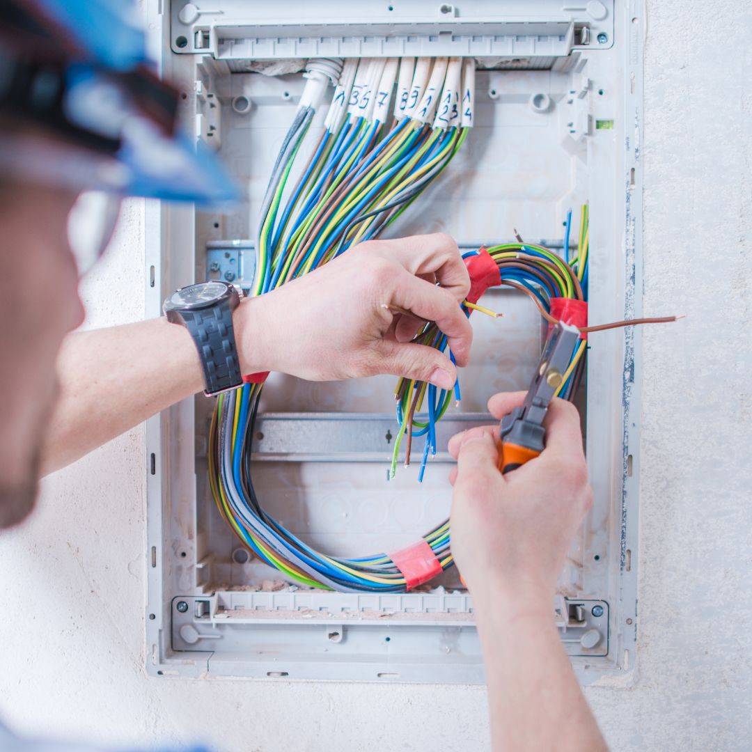 Electrician working on boat electrical panel, managing colorful wires and connections, emphasizing power management and automation solutions for yacht electrical systems.