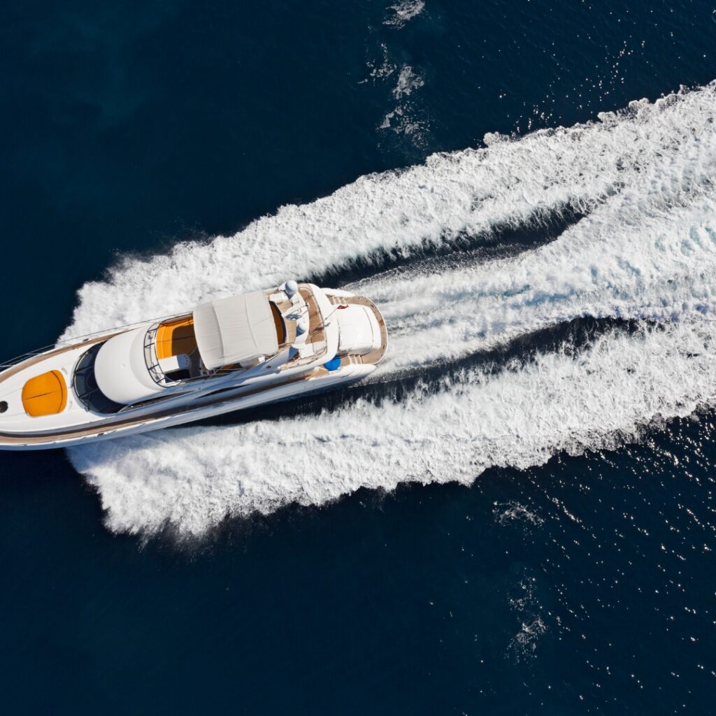 Luxury yacht navigating through vibrant blue waters, leaving a wake, representing peak performance and maintenance services at Safe Harbor Savannah Yacht Center.