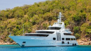 Luxury yacht anchored in serene waters near lush green hills, representing marine electrical services and yachting experiences in Savannah, Georgia.
