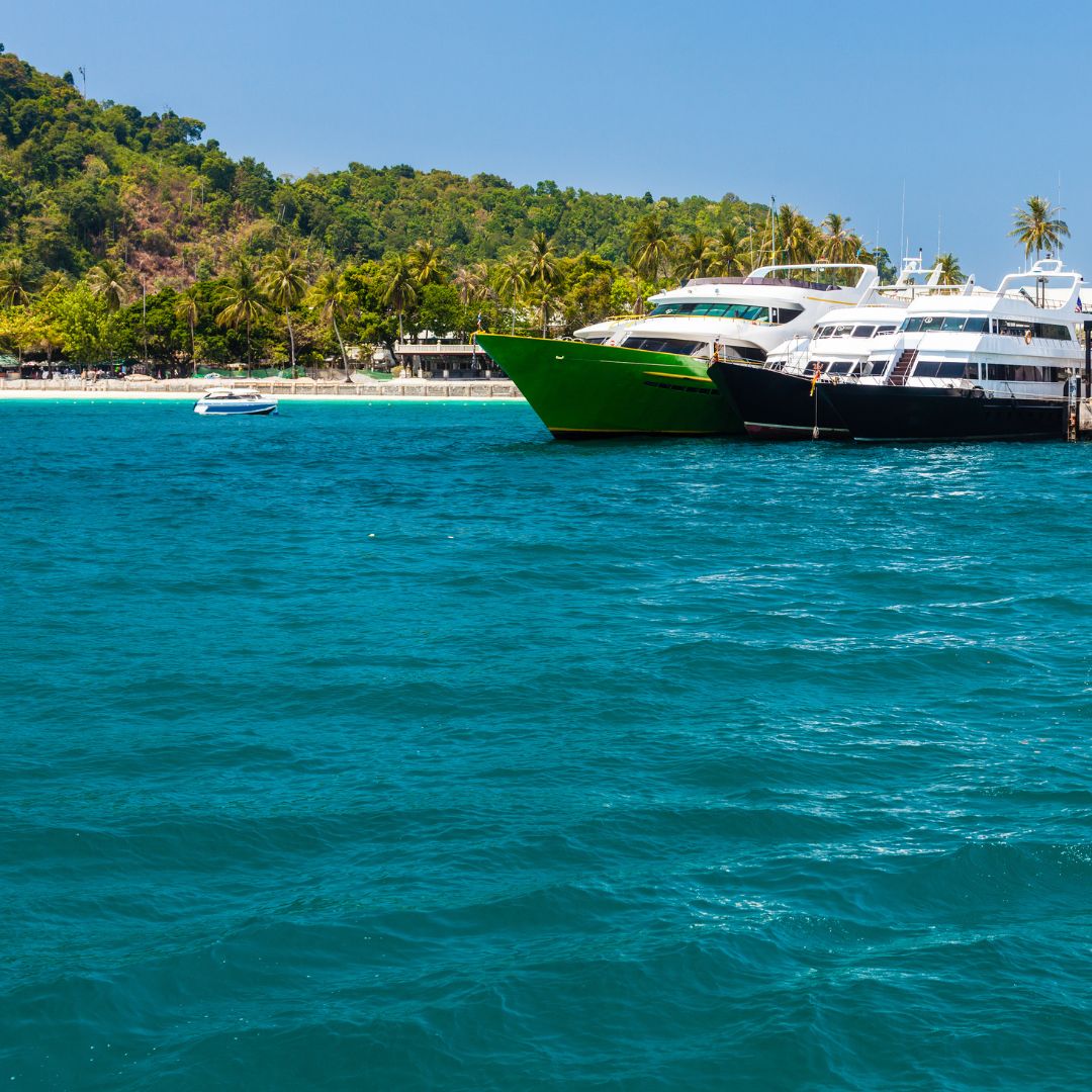 Yachts docked along the Amalfi Coast with vibrant green and black hulls, surrounded by clear blue waters and lush greenery.