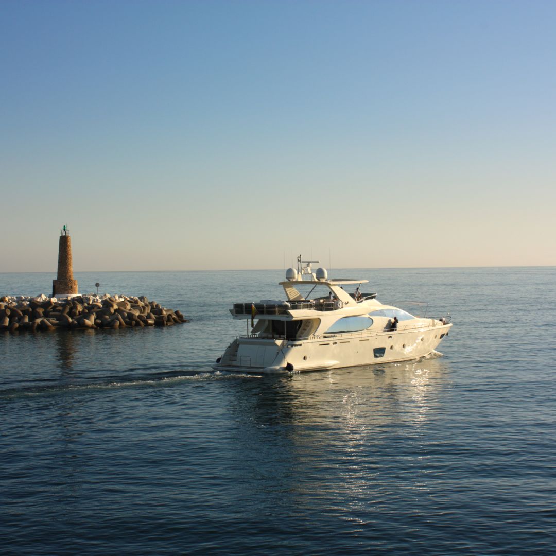 Luxury yacht navigating calm waters near a stone lighthouse, symbolizing premier electrical services for yachts in Monaco.